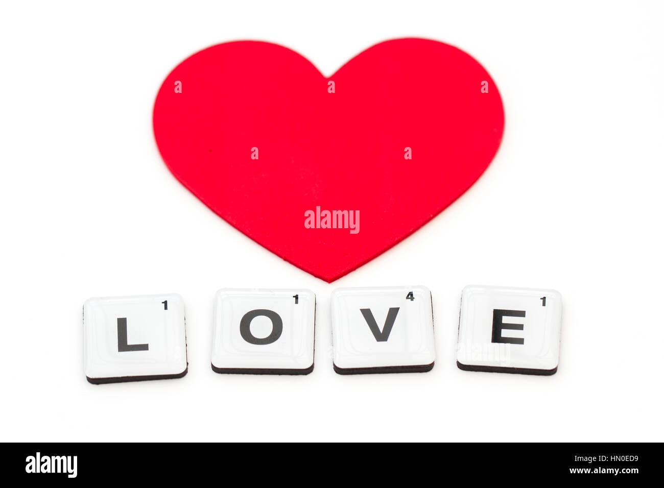 La parola amore ha creato dalla lettera piazze o piastrelle scrabble isolato su un fondo bianco con cuori e copia di spazio. Foto Stock