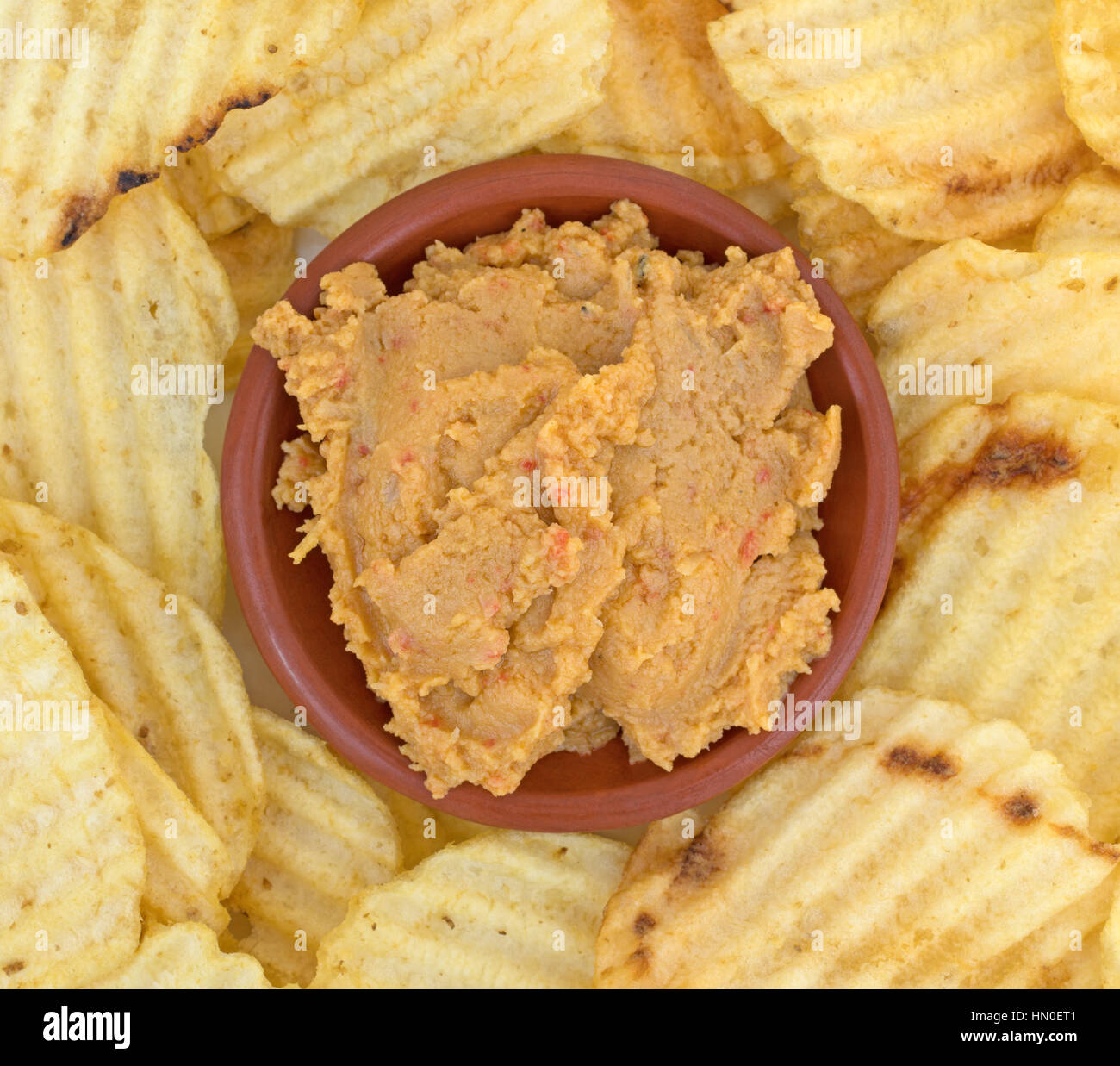 Top vista ravvicinata di una piccola ciotola di hummus salsa di carciofi con patate fritte che circonda il recipiente su una piastra. Foto Stock
