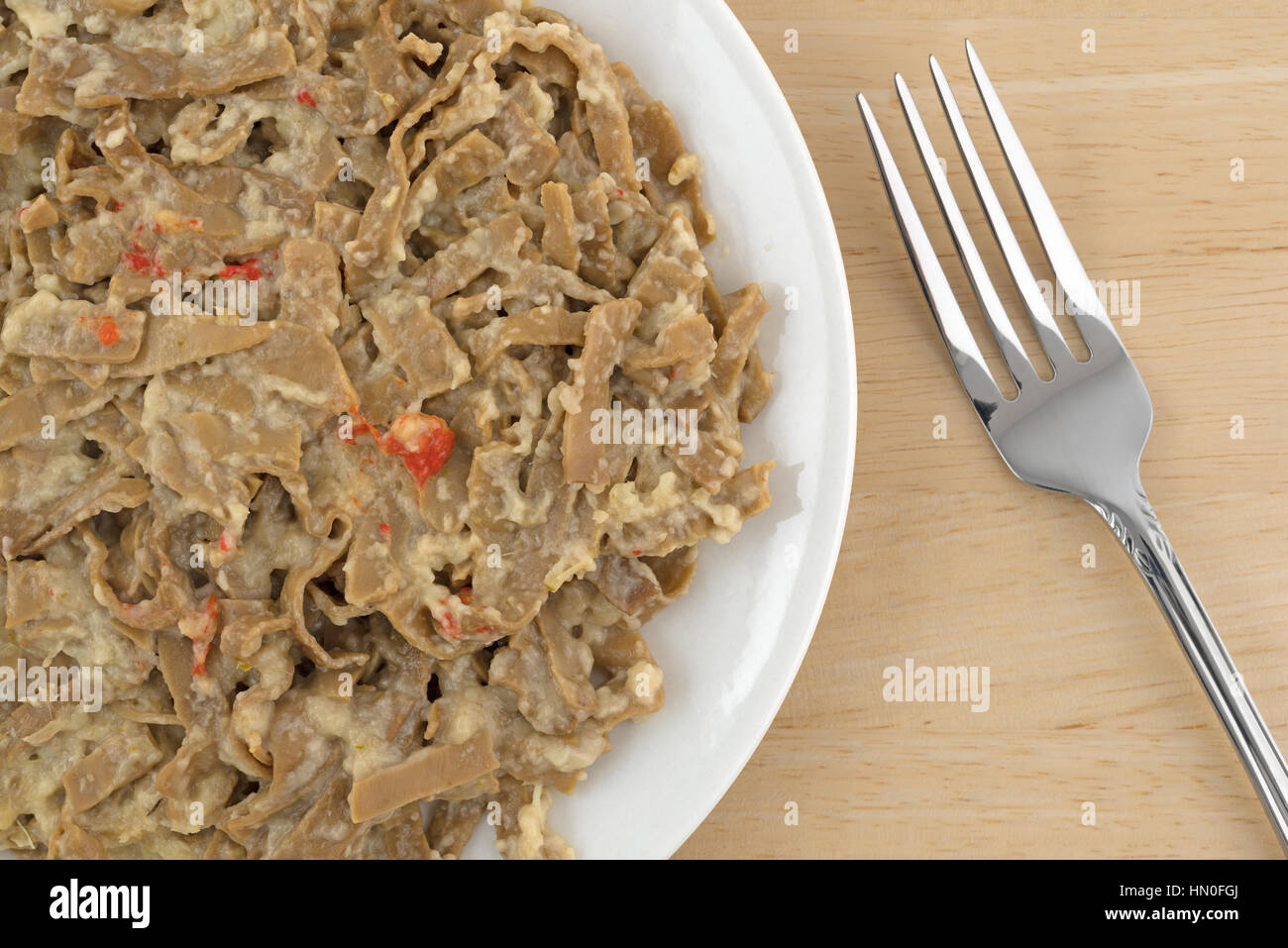 Top vista ravvicinata di un serving di edamame fettuccine con una salsa di cocco su una piastra con una forcella per il lato in cima a una tavola di legno alto. Foto Stock