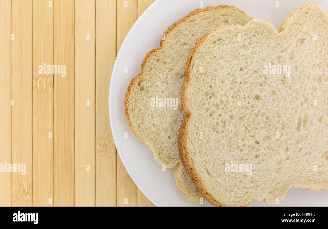 Top vista ravvicinata di due fette di muffin inglese Come tostare il pane su una piastra in cima a un luogo di legno mat. Foto Stock