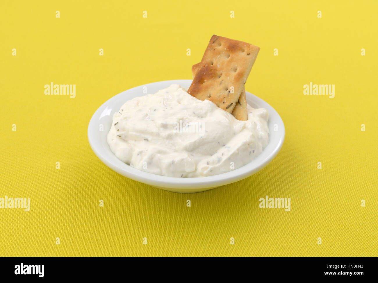 Il rosmarino e olio di oliva aromatizzato cracker inserito in francese dip di cipolla in una piccola ciotola su un luminoso giallo tovaglia. Foto Stock