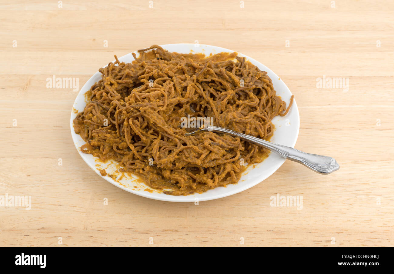 A che serve di soia spaghetti con sugo di pomodoro su una piastra con un cucchiaio inserita nel cibo in cima a una tavola di legno. Foto Stock