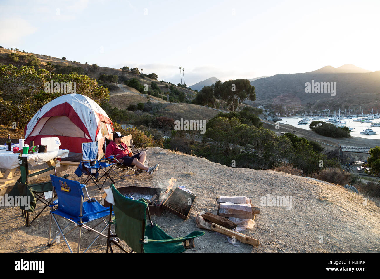 Un uomo si rilassa a camp come il sole tramonta su due porti sull isola Catalina. Foto Stock