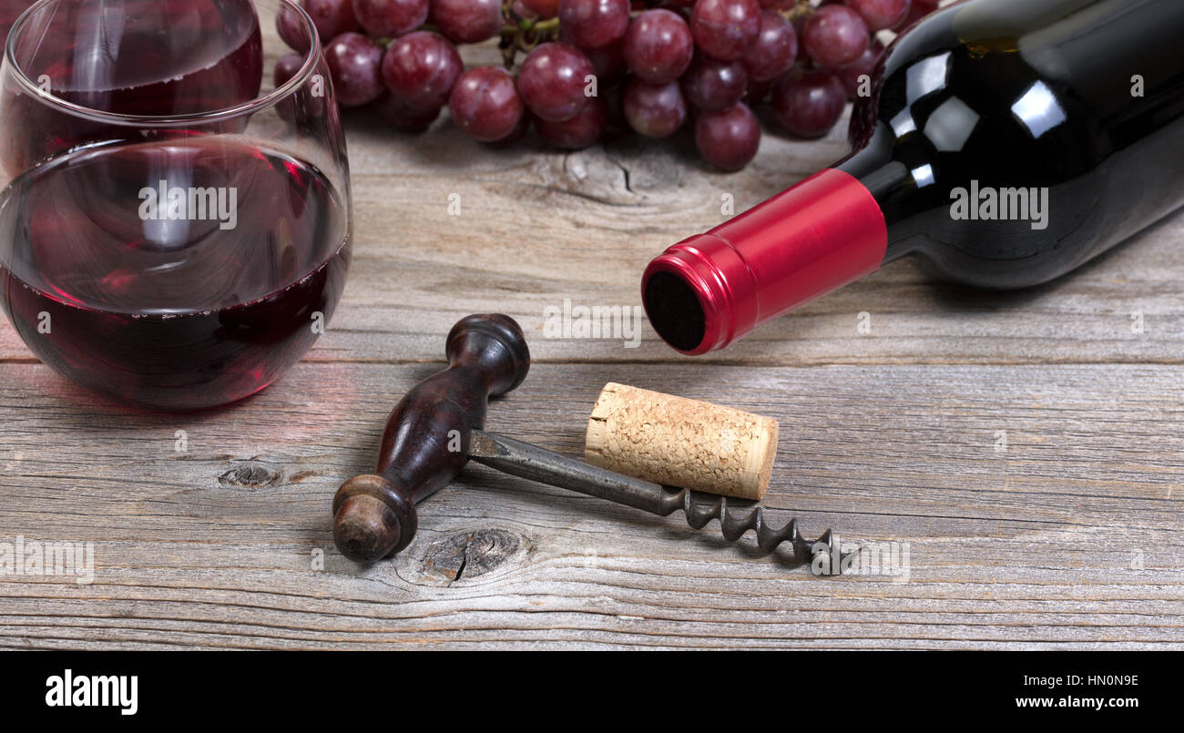 Messa a fuoco selettiva su vintage cavatappi con una bottiglia di vino rosso, uva e bicchieri in background su rustiche tavole in legno Foto Stock