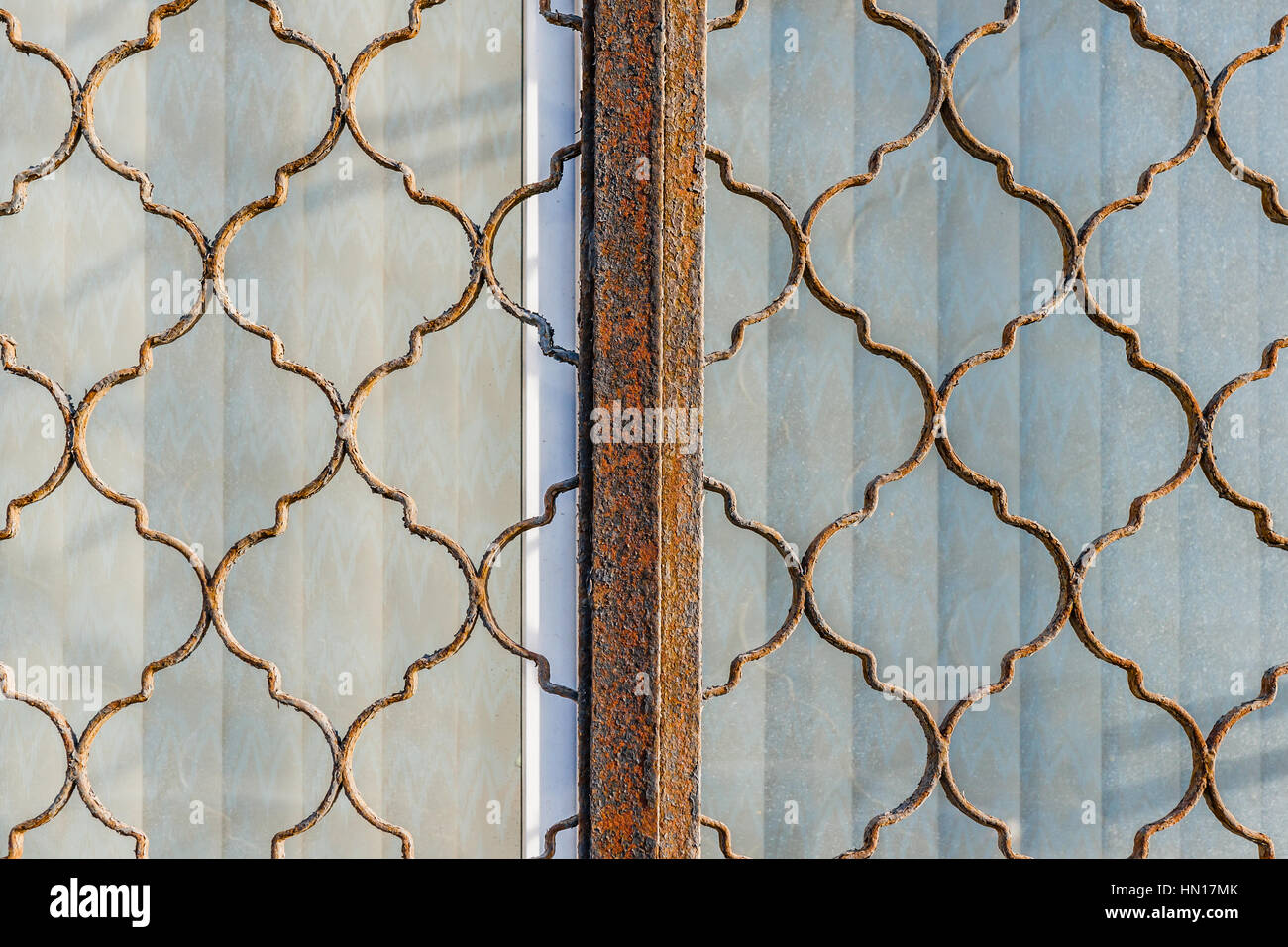 Vista ingrandita di spalliere di rusty a forma di reticolo di metallo, lattice o reja su una finestra accecato con stringa tende. È tutto chiuso e protetto. Foto Stock