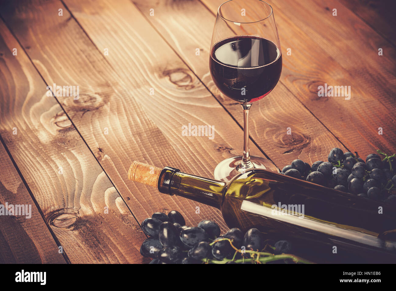 Bottiglia e bicchiere di vino rosso, uva e sughero su sfondo di legno Foto Stock