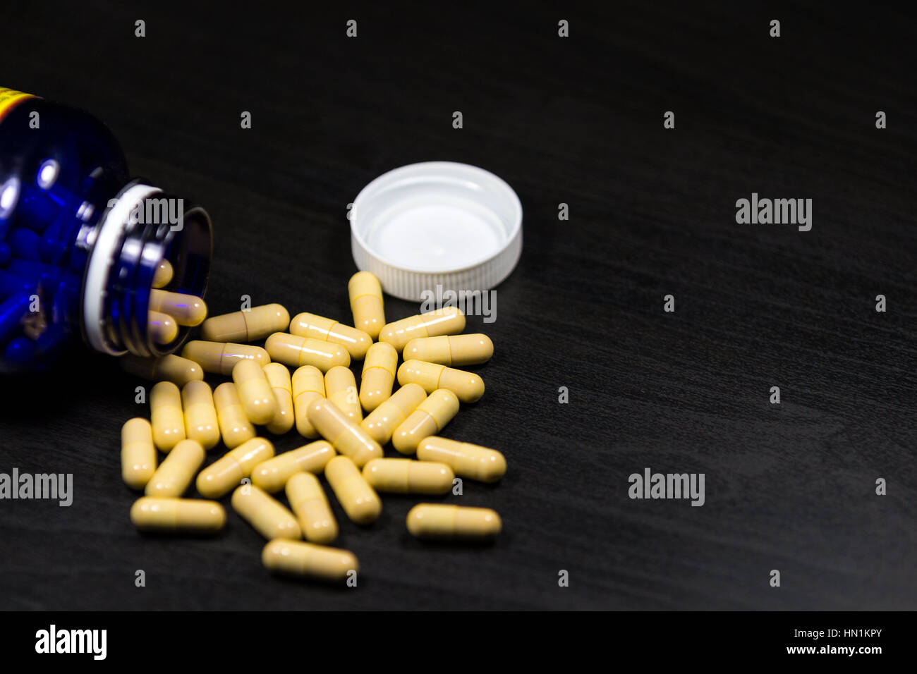 Pillola bottiglia versarsi pillole sulla superficie isolata su uno sfondo nero Foto Stock