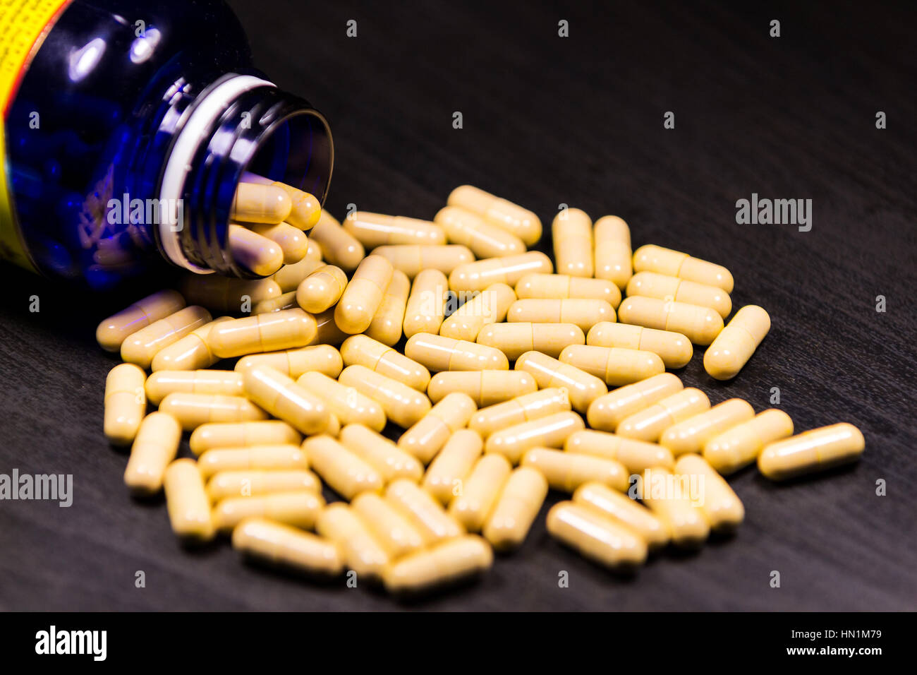 Pillola bottiglia versarsi pillole sulla superficie isolata su uno sfondo nero Foto Stock
