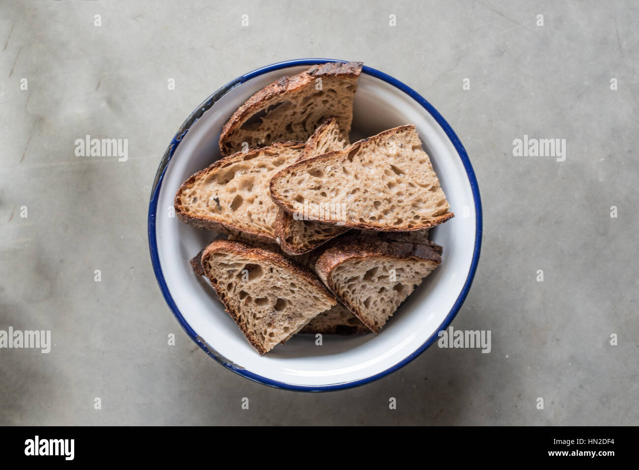 Fette di pane appena sfornato pane di pasta acida in un bianco e blu ciotola su un sfondo tondi per cemento Foto Stock