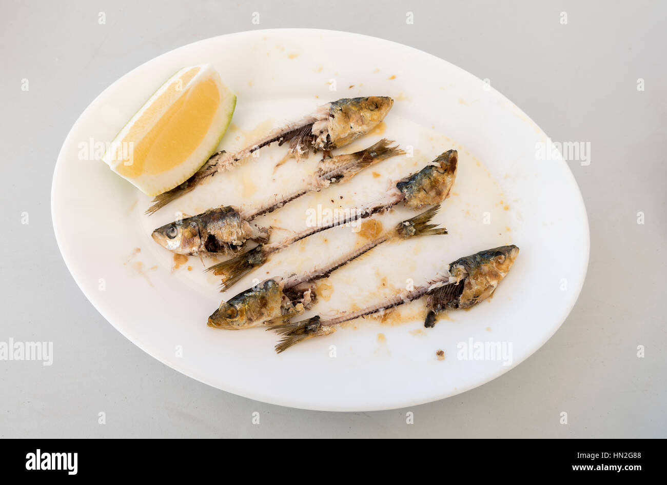 I resti di un piatto di sardine, con le ossa, la testa e la coda del pesce visibile, insieme con una fetta di limone. Foto Stock