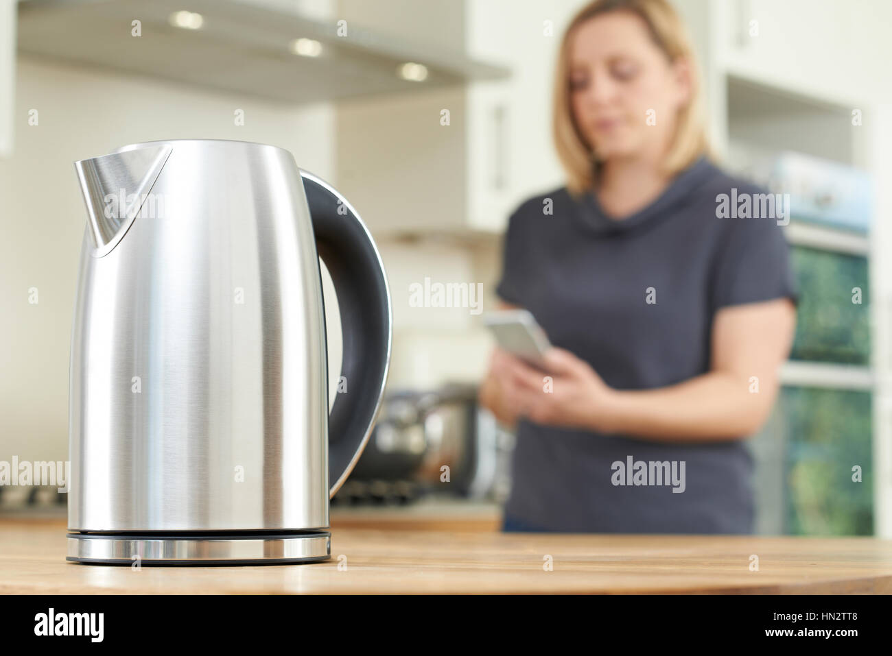 La donna il controllo Smart bollitore utilizzando App sul telefono cellulare Foto Stock