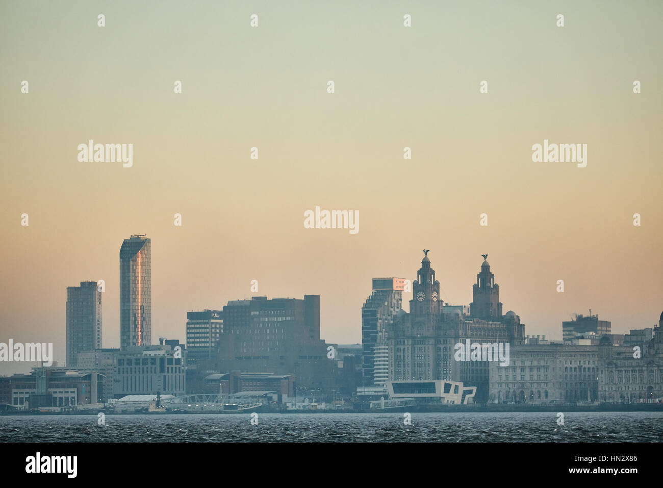 Da Birkenhead lato del fiume Mersey guardando verso il cielo arancione tramonto sul centro di Liverpool landmark waterfront skyline nel Merseyside, Foto Stock