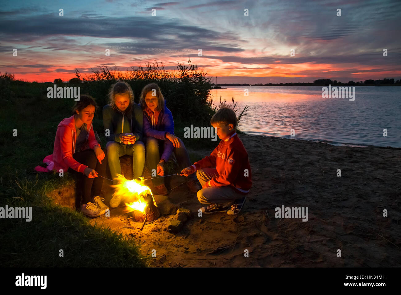 Madre e tre bambini tostatura di marshmallows nel falò sulla riva al tramonto Foto Stock