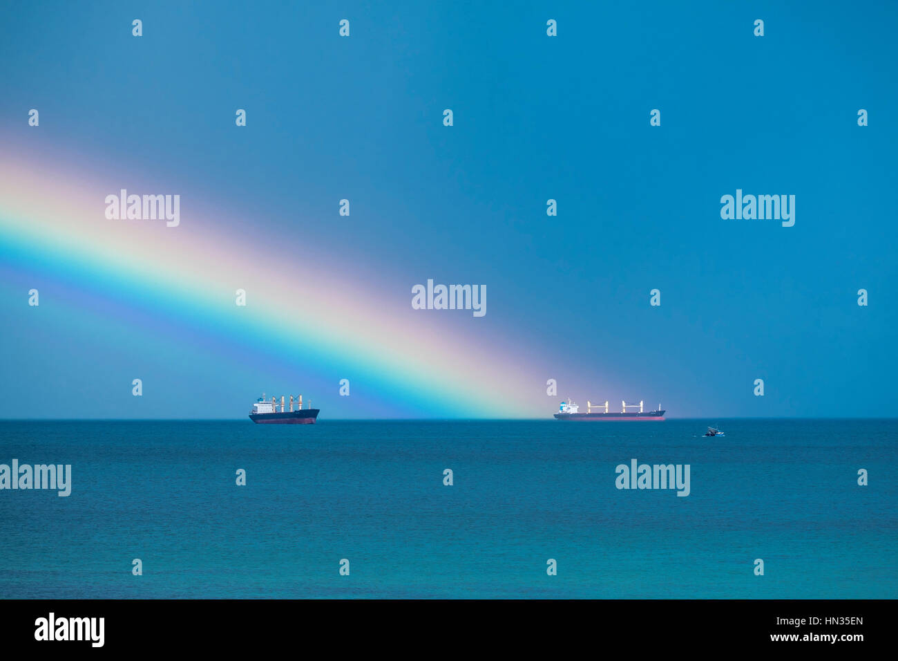 Un arcobaleno in mare e di due navi container al di ancoraggio. Foto Stock