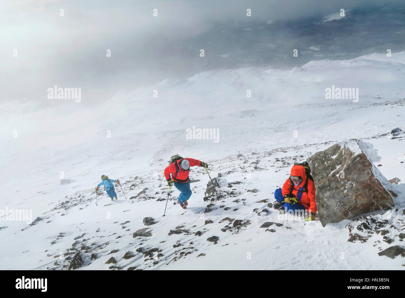 Un uomo è tenuto un riparo contro il vento dietro una roccia durante un Backcountry Ski Tour Foto Stock