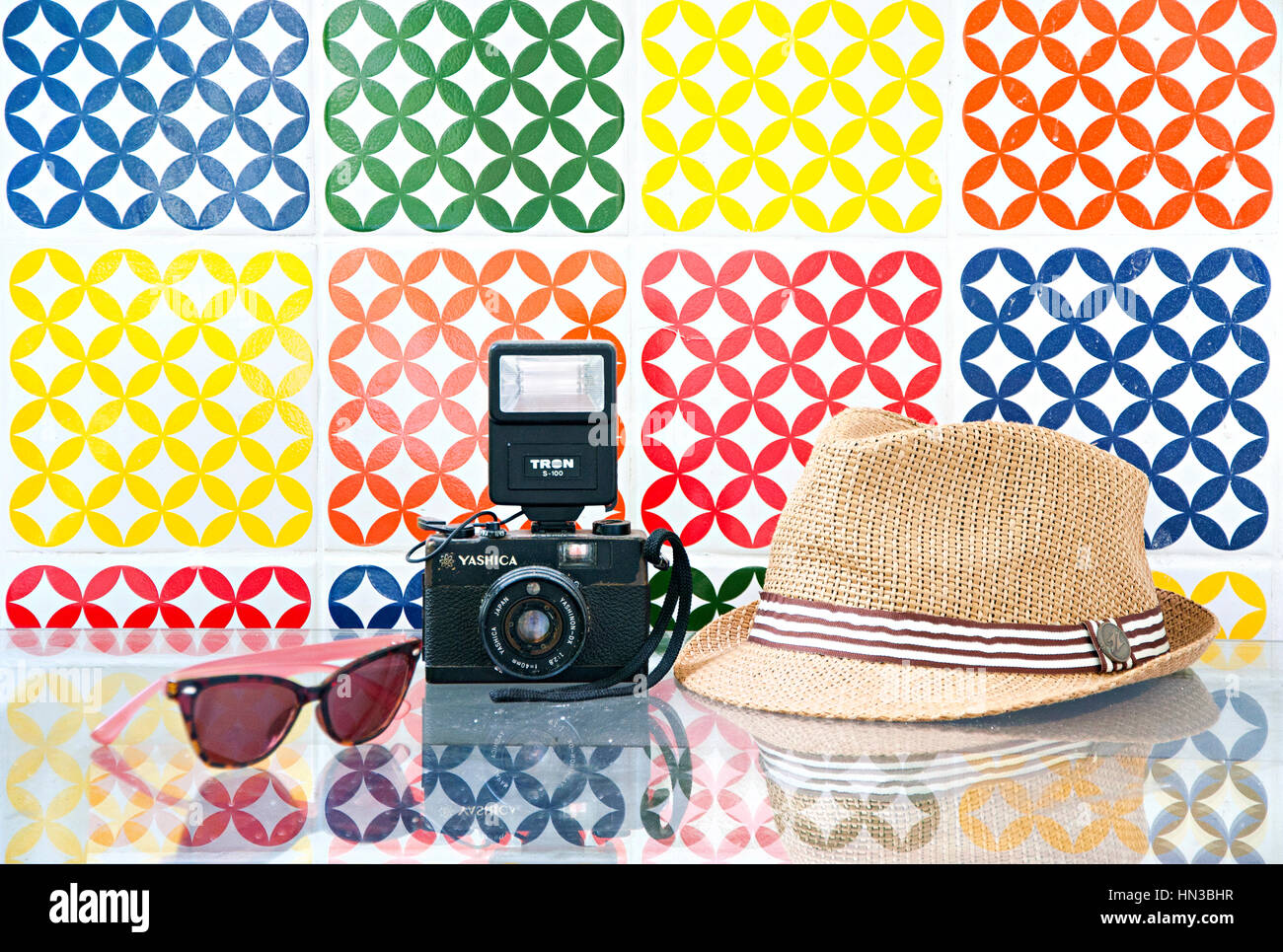 Viaggiare con cappello di fotocamera e occhiali con una grafica colorata Tile parete dietro Foto Stock