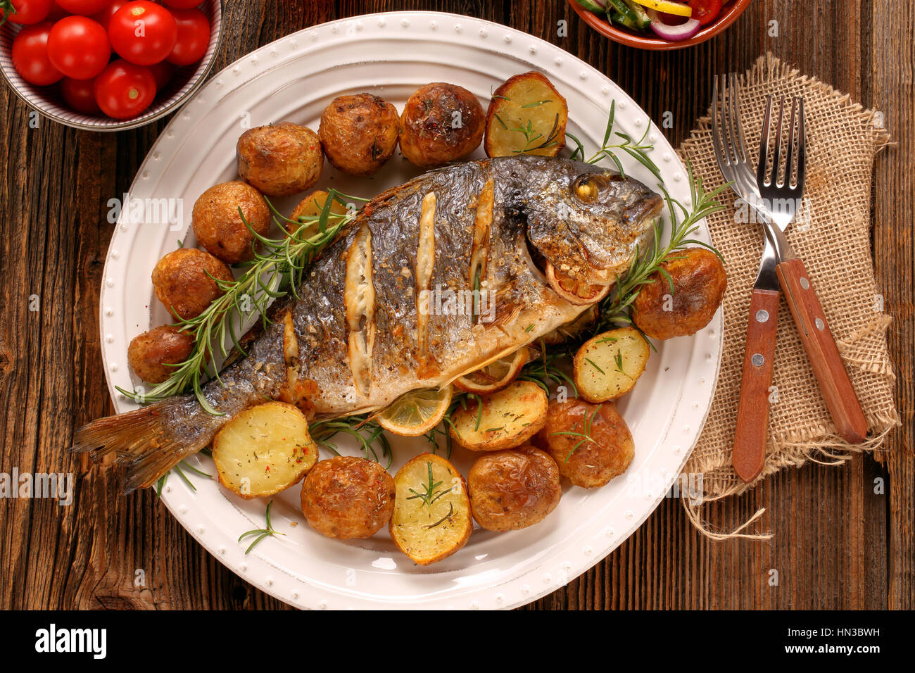 Pesce alla griglia con patate arrosto e verdure sulla piastra Foto Stock