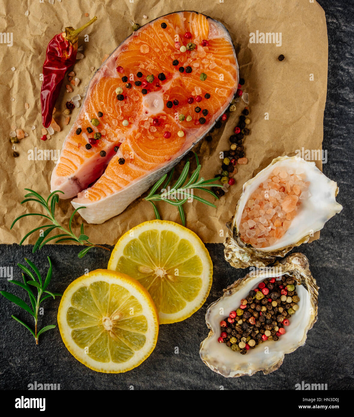 Deliziosa bistecca di salmone , ricco di omega 3 olio con erbe aromatiche e spezie con un limone, pomodoro, aglio su sfondo nero. Un sano e la dieta alimentare. Foto Stock