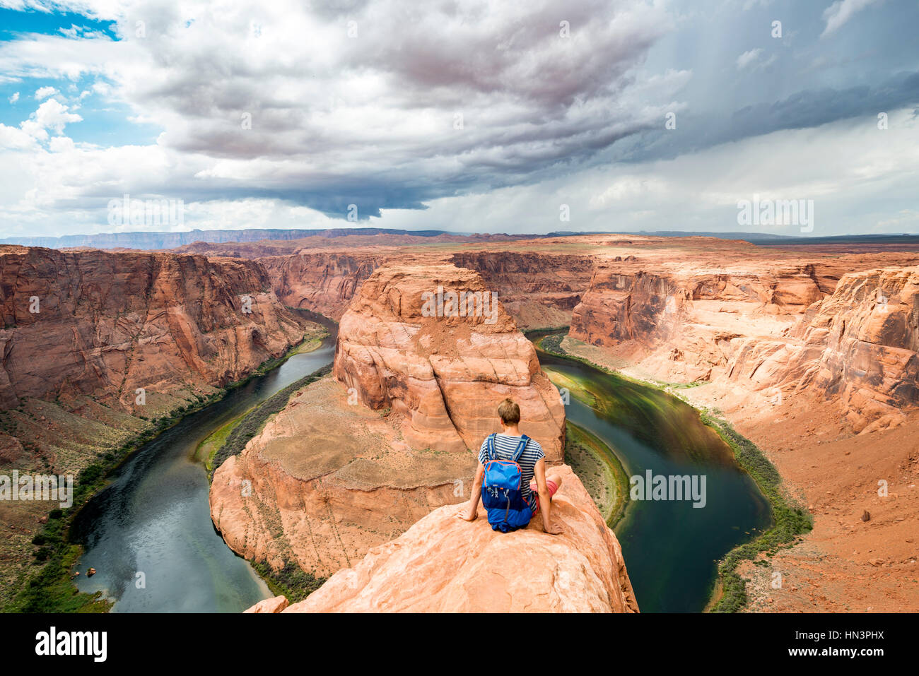 Giovane uomo seduto su di una roccia a ferro di cavallo curva, ansa del fiume Colorado, re Bend, Glen Canyon National Recreation Area, pagina Foto Stock