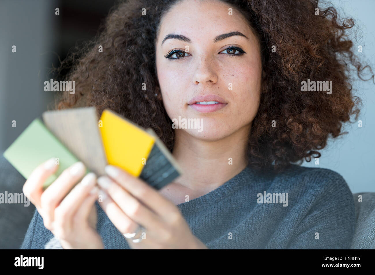 Riflessivo naturale giovane donna guardando la telecamera con un espressione lontani come lei si mantiene una manciata di campioni di legno per la decorazione della casa Foto Stock