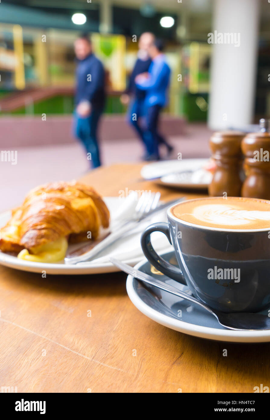 Close-up di caffè e croissant sulla tavola in una caffetteria con persone sfocate come sfondo Foto Stock
