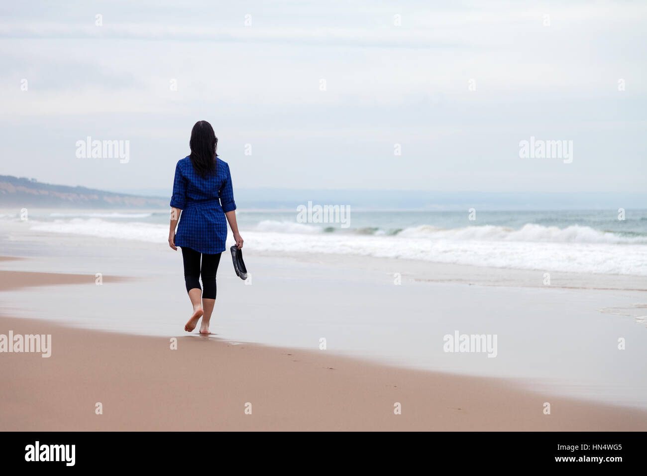 Giovane donna che cammina da sola in una spiaggia deserta in un giorno d'autunno / donna che cammina da sola tristezza triste depressione depressa malinconica Foto Stock