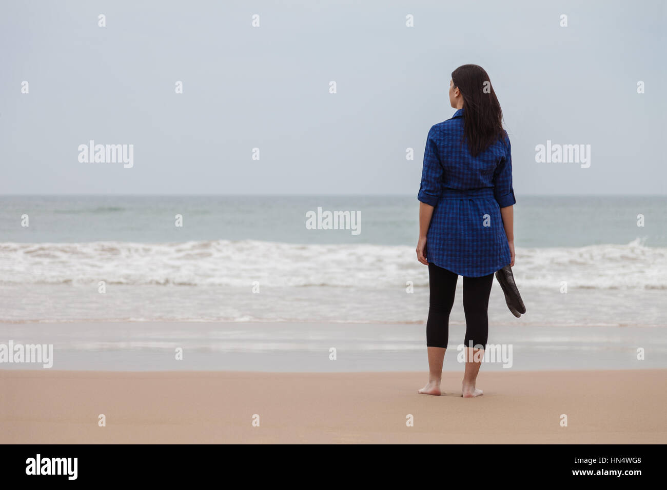 Solitaria e premuto donna in piedi di fronte al mare in una spiaggia deserta in una giornata autunnale / donna spiaggia da sola lonely triste tristezza premuto Foto Stock