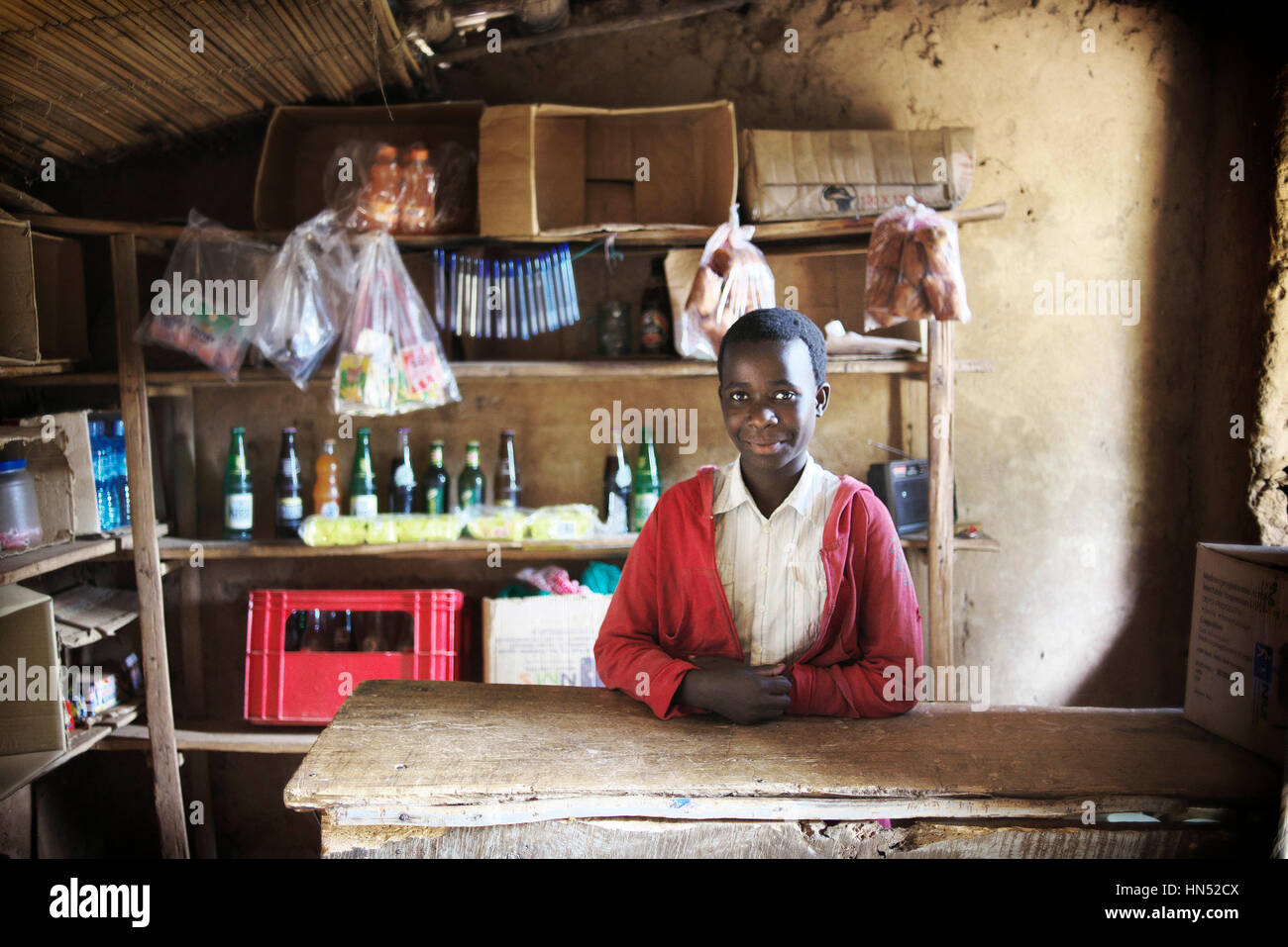 Giovane ragazza ugandese vestito in uniforme scolastica comporta per un ritratto in locali del negozio del villaggio Foto Stock