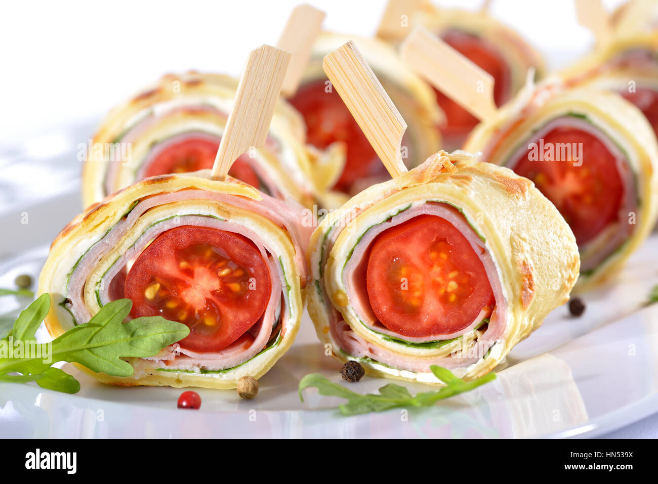 Deliziosi stuzzichini: rotoli di frittelle sottili (crepes) con prosciutto, formaggio spalmabile, insalata di rucola e pomodorini Foto Stock