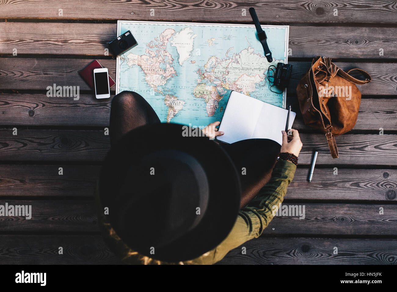 Vista superiore della donna che indossa hat facendo tour piano utilizzando una mappa del mondo. Tourist esplorando la mappa del mondo con accessori da viaggio intorno a. Foto Stock