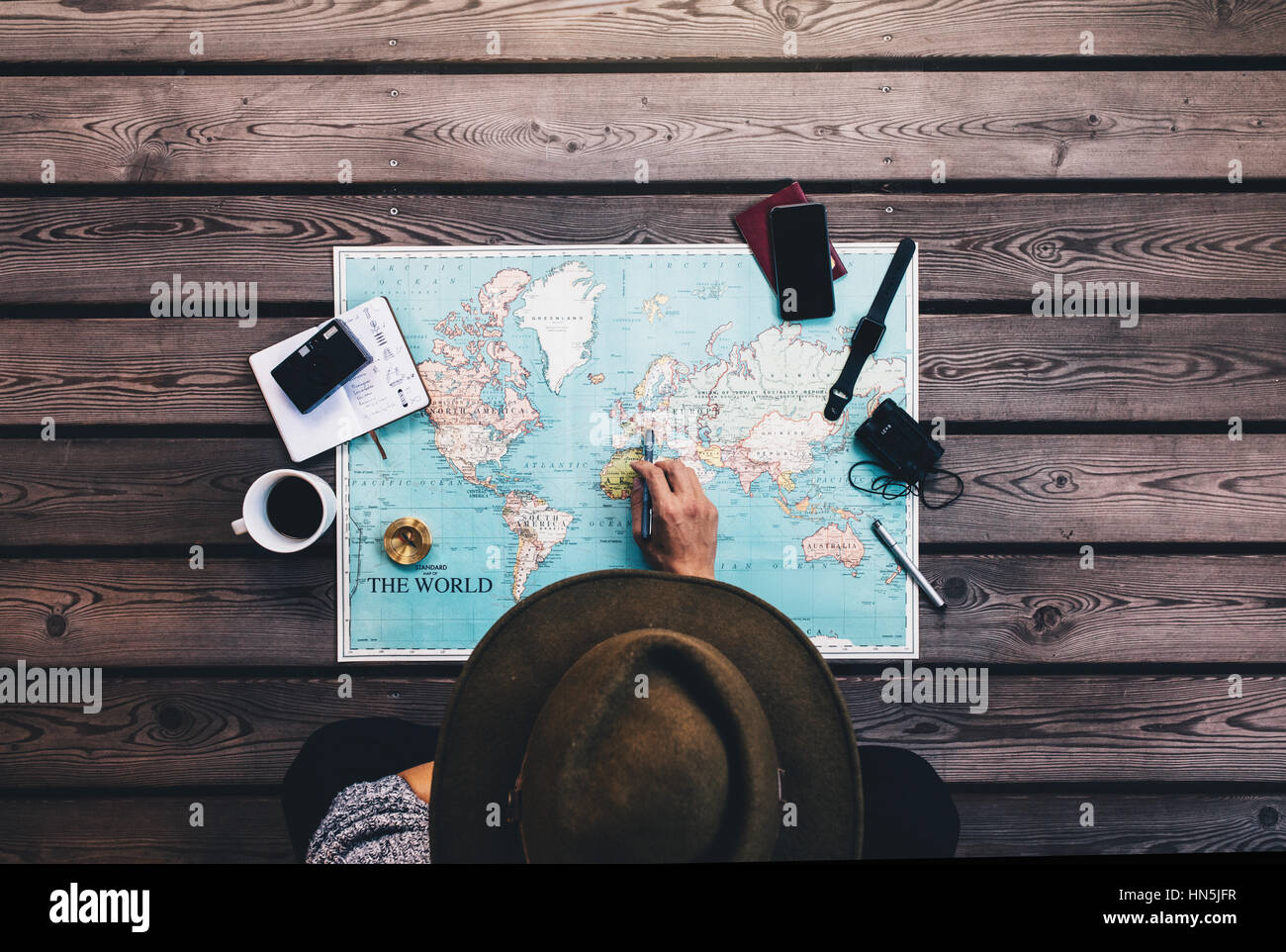 Puntamento turistica in Europa sulla mappa del mondo circondato con il binocolo, Bussola e altri accessori da viaggio. Uomo che indossa marrone cappello pianificazione il suo look tour Foto Stock