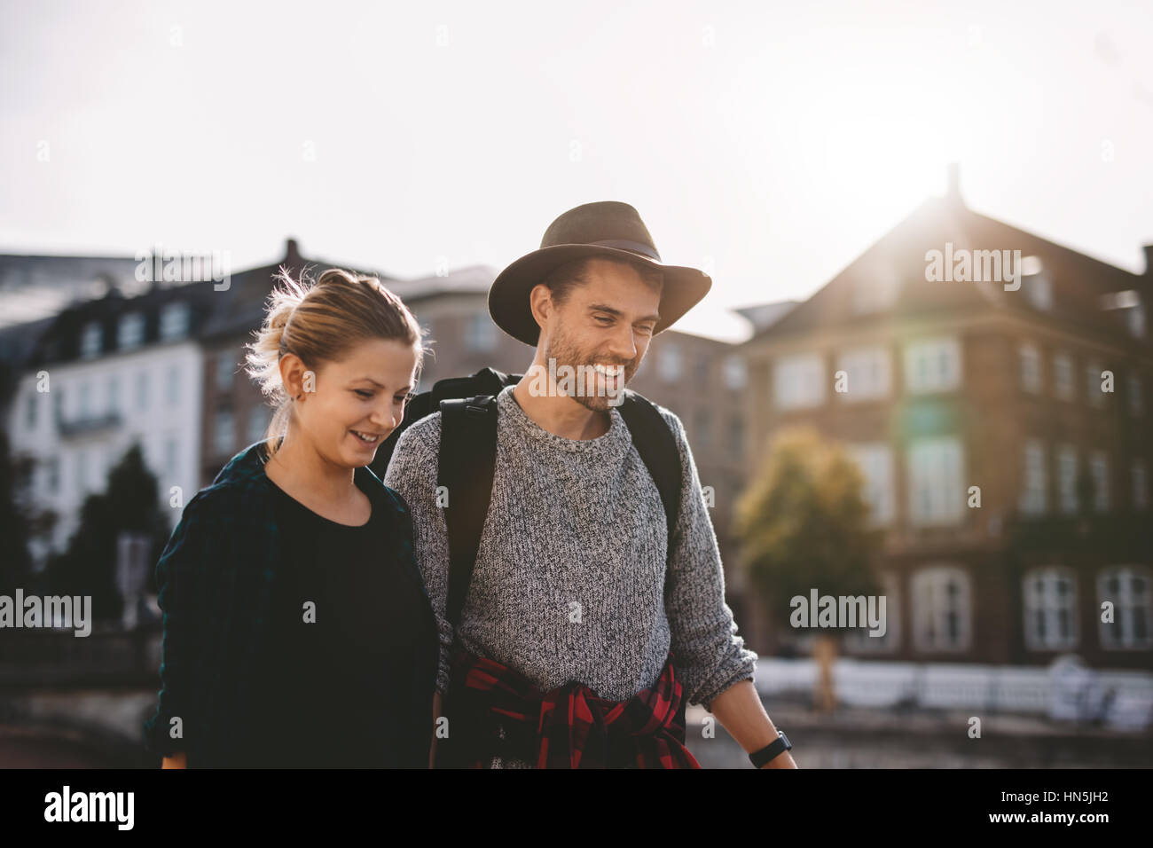 Sorridente una giovane coppia in vacanza a piedi su strada con la luce del sole in background. Foto Stock
