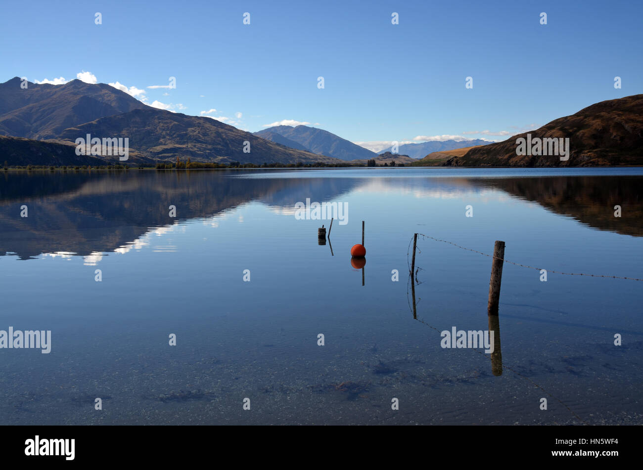 Il lago Wanaka riflessioni in autunno. In primo piano è un relitto recinzione e boa arancione. Otago, Nuova Zelanda. Foto Stock