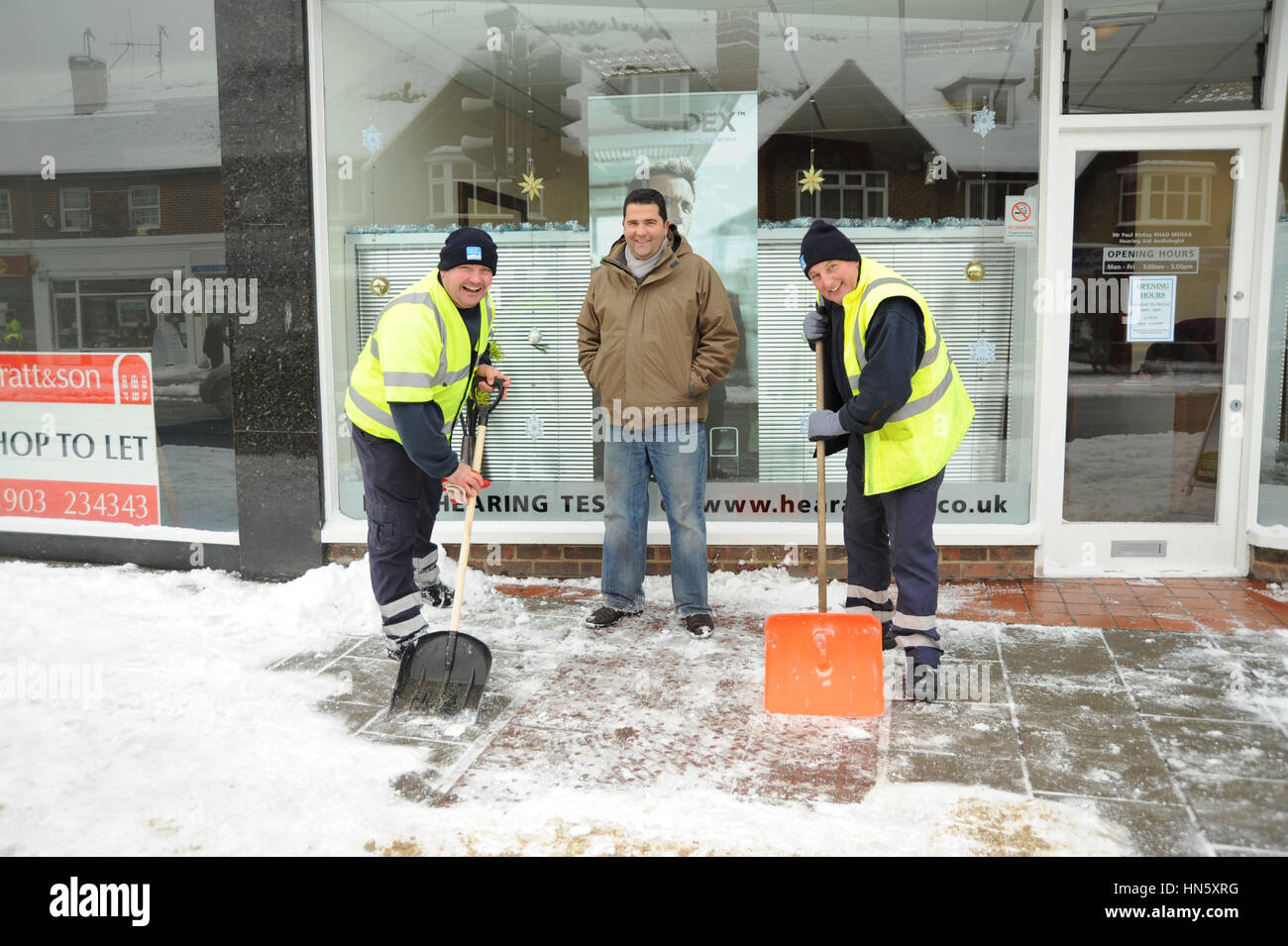 Gli uomini la rimozione di neve da un marciapiede davanti a un negozio a Worthing Foto Stock