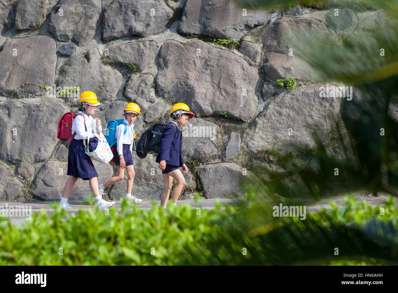 Sakura-jima, Giappone - 23 Aprile 2012: tre scolari a casa a piedi Indossare copricapi rigidi per proteggere contro potenzialmente pericolosi detriti da Sakura-jima Foto Stock