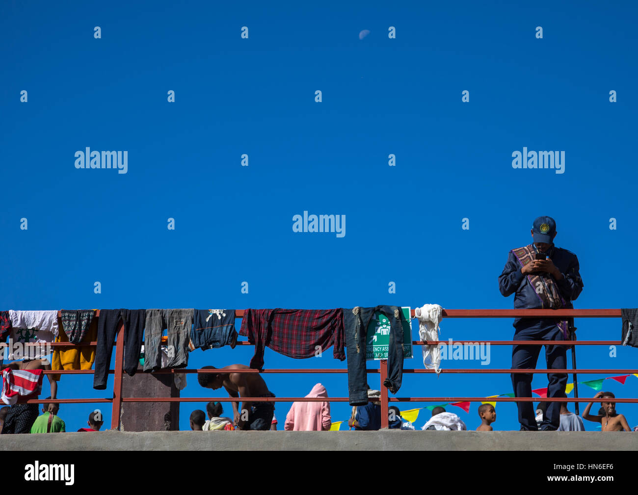 Poliziotto etiope guardando al suo telefono cellulare mentre la gente asciugare i loro abiti dopo il bagno santo durante il festival Timkat, Amhara Region, Lalibela, Et Foto Stock