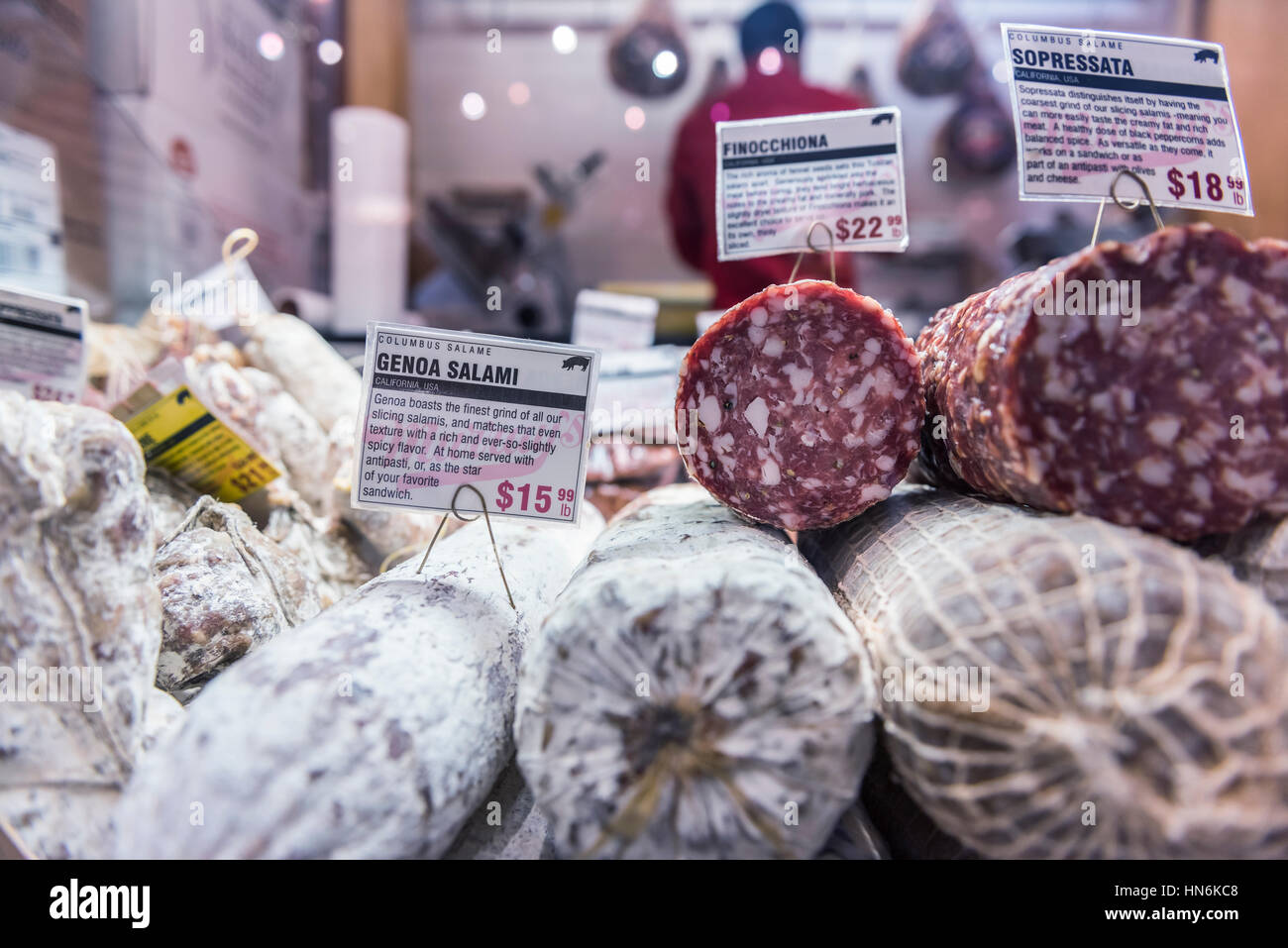 Primo piano della sopressata e salame di genova rulli sul display in un mercato con negozio di macellaio in background Foto Stock