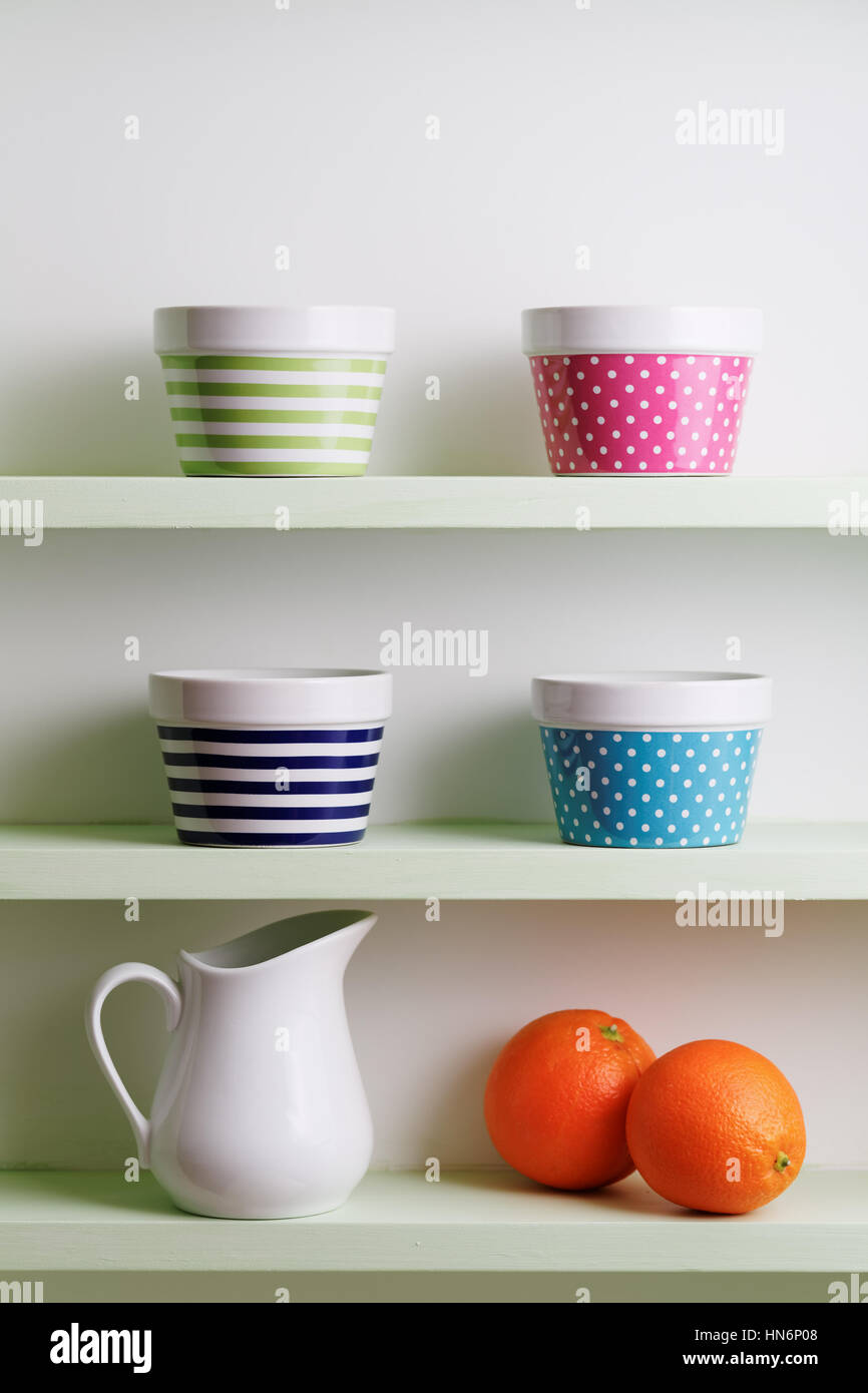 Tazze colorate su un ripiano della cucina. Una cucina scaffalatura tenendo a strisce e spotted bocce. Mensola da cucina disposizione. Foto Stock