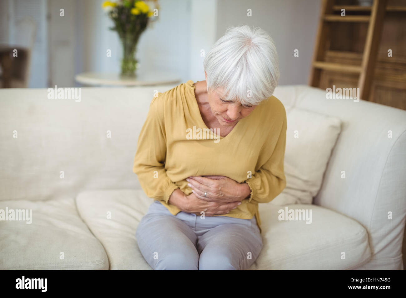 Senior donna che soffre di dolori di stomaco nel salotto di casa Foto Stock