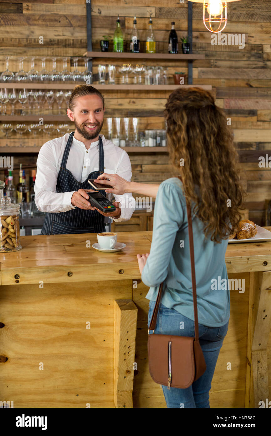 La donna il pagamento fattura tramite lo smartphone utilizzando la tecnologia NFC in cafe Foto Stock