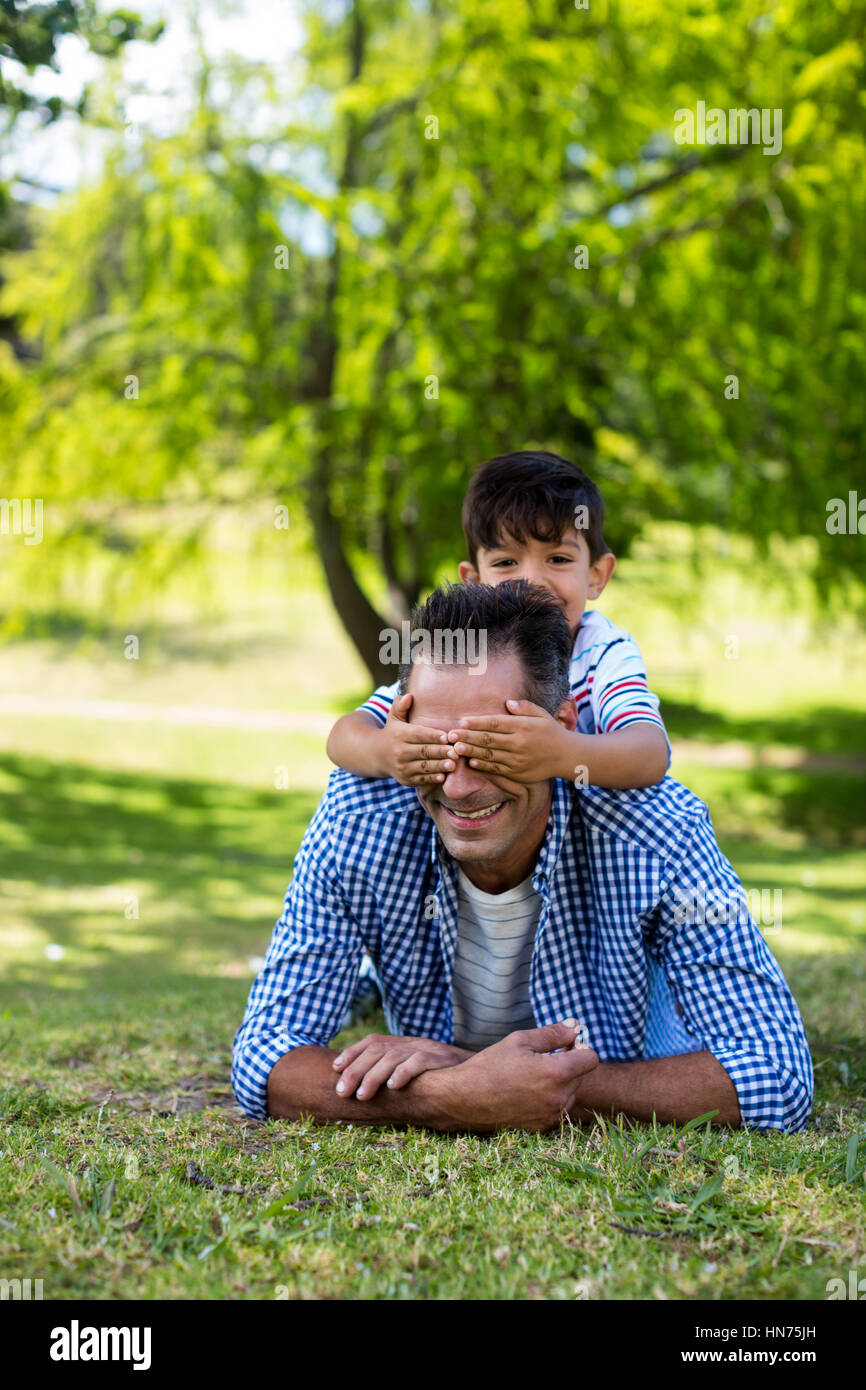 Ragazzo che copre la sua gli occhi dei padri in park in una giornata di sole Foto Stock