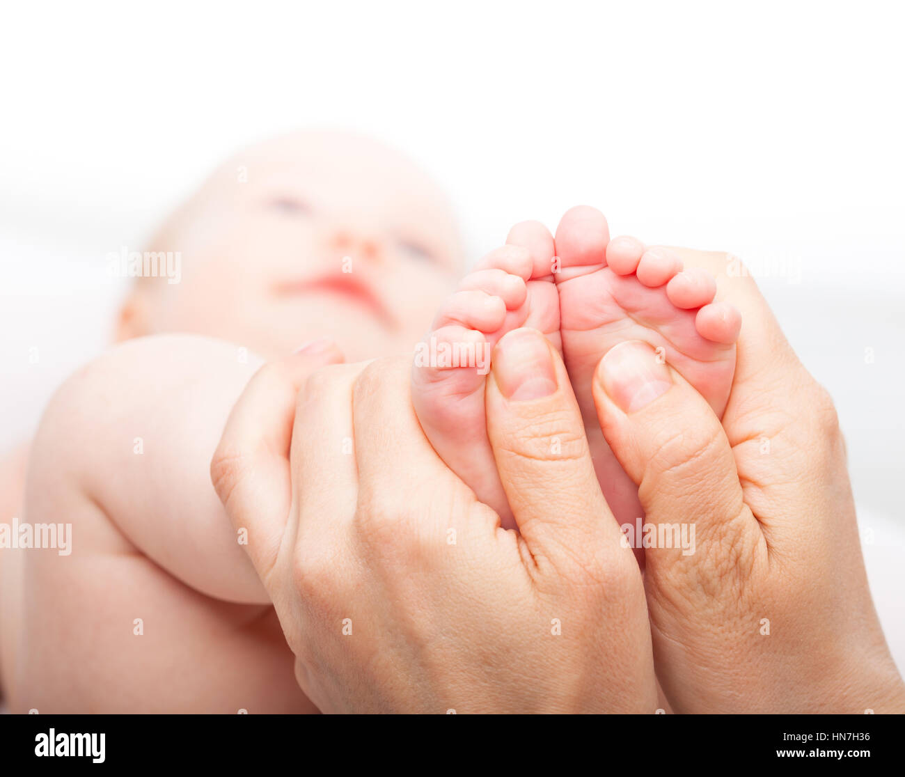 Close-up shot di tre mese bambina ricevere massaggio ai piedi da una femmina terapista di massaggio. La fotocamera è focalizzata sul neonato i piedi. La faccia è offuscata nel Foto Stock