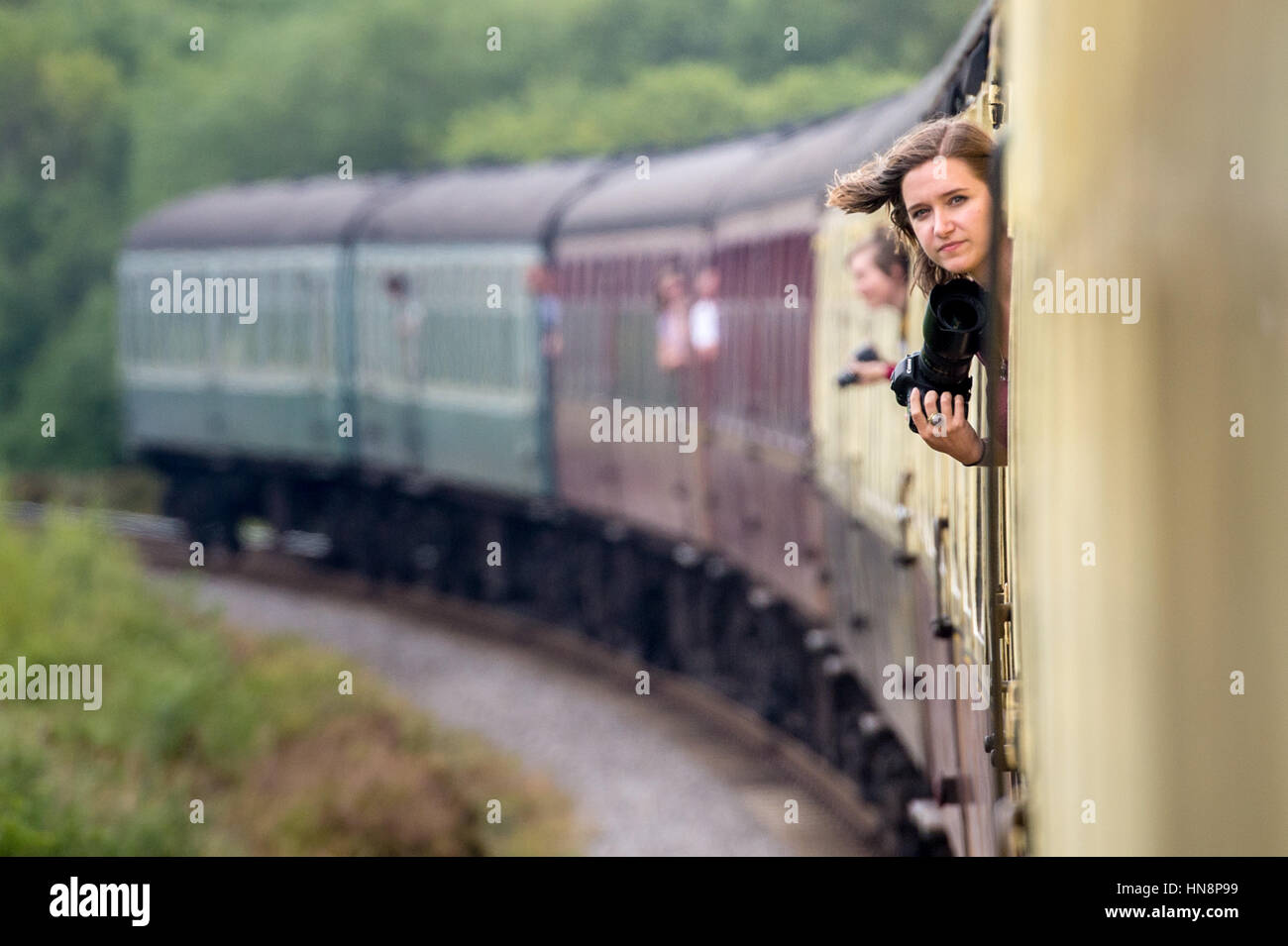 Regno Unito, Inghilterra, Yorkshire - Giovane donna bloccata la sua testa fuori di un treno in movimento con la sua macchina fotografica in viaggio verso il basso il North Yorkshire Moors Railw storico Foto Stock