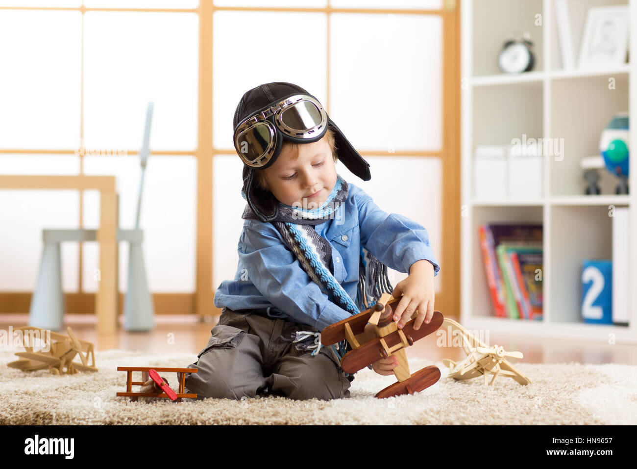 Kid boy usurata aviatore casco gioca con il giocattolo di legno piani nella sua camera per bambini Foto Stock