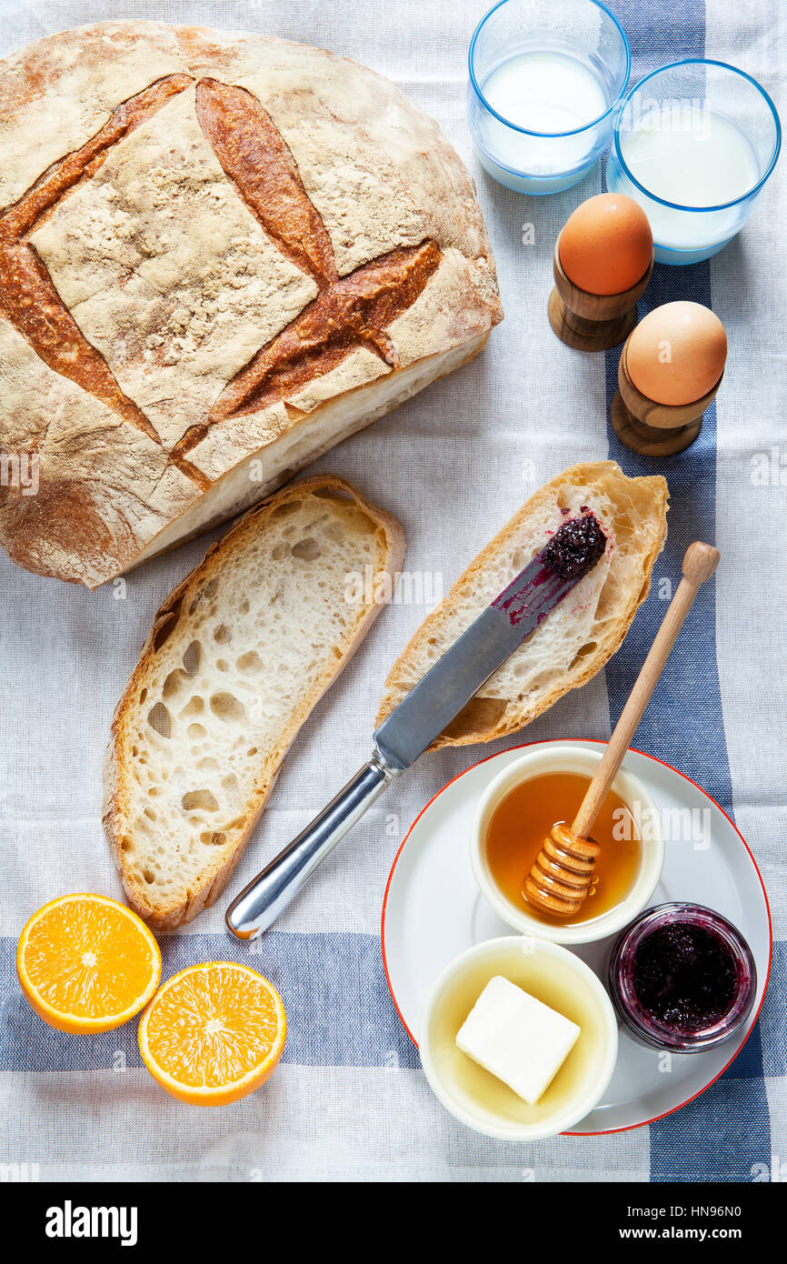 Tavolo per la colazione. Pane, uova sode, burro, miele, marmellata, arance, latte Foto Stock