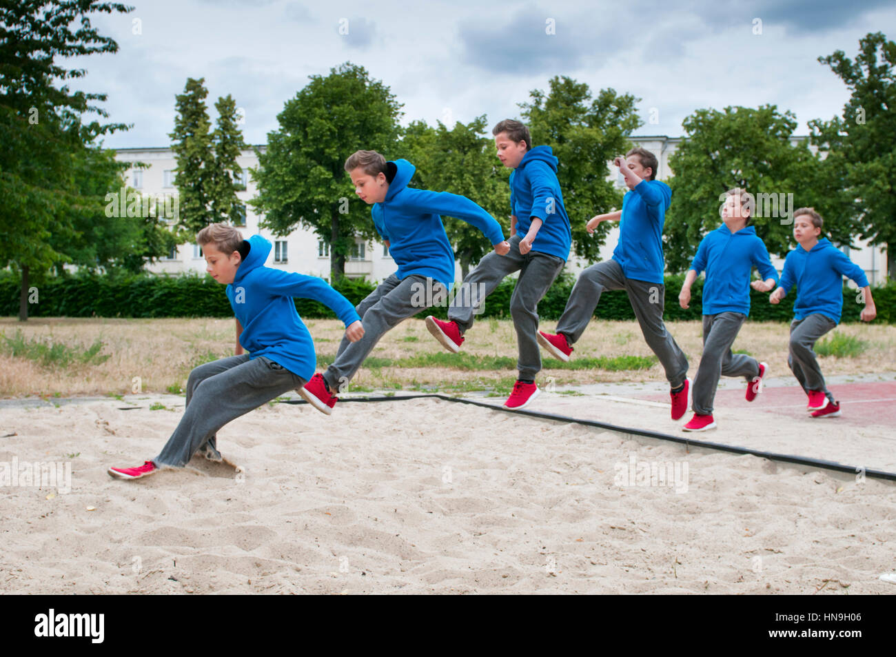 Colpo di sequenza di un adolescente di sesso maschile in giacca blu e pantaloni  grigi quando si salta in un salto in lungo pit Foto stock - Alamy