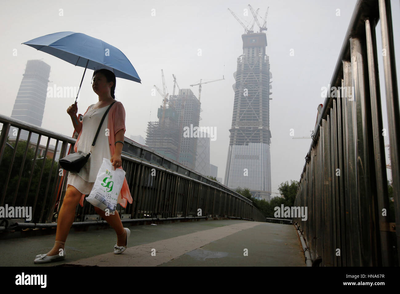 Una donna con ombrellone passa alti edifici in costruzione su un vago giorno, dovute all'inquinamento, a Pechino, Cina, Venerdì 29 Luglio, 2016 Pho Foto Stock