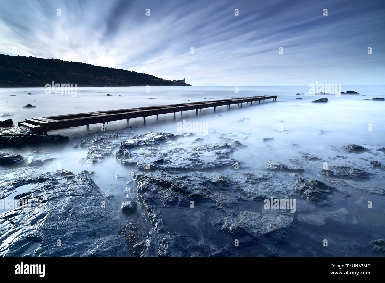 Il molo di legno o un pontile e scogli su un oceano blu al mattino. Esposizione lunga Foto Stock