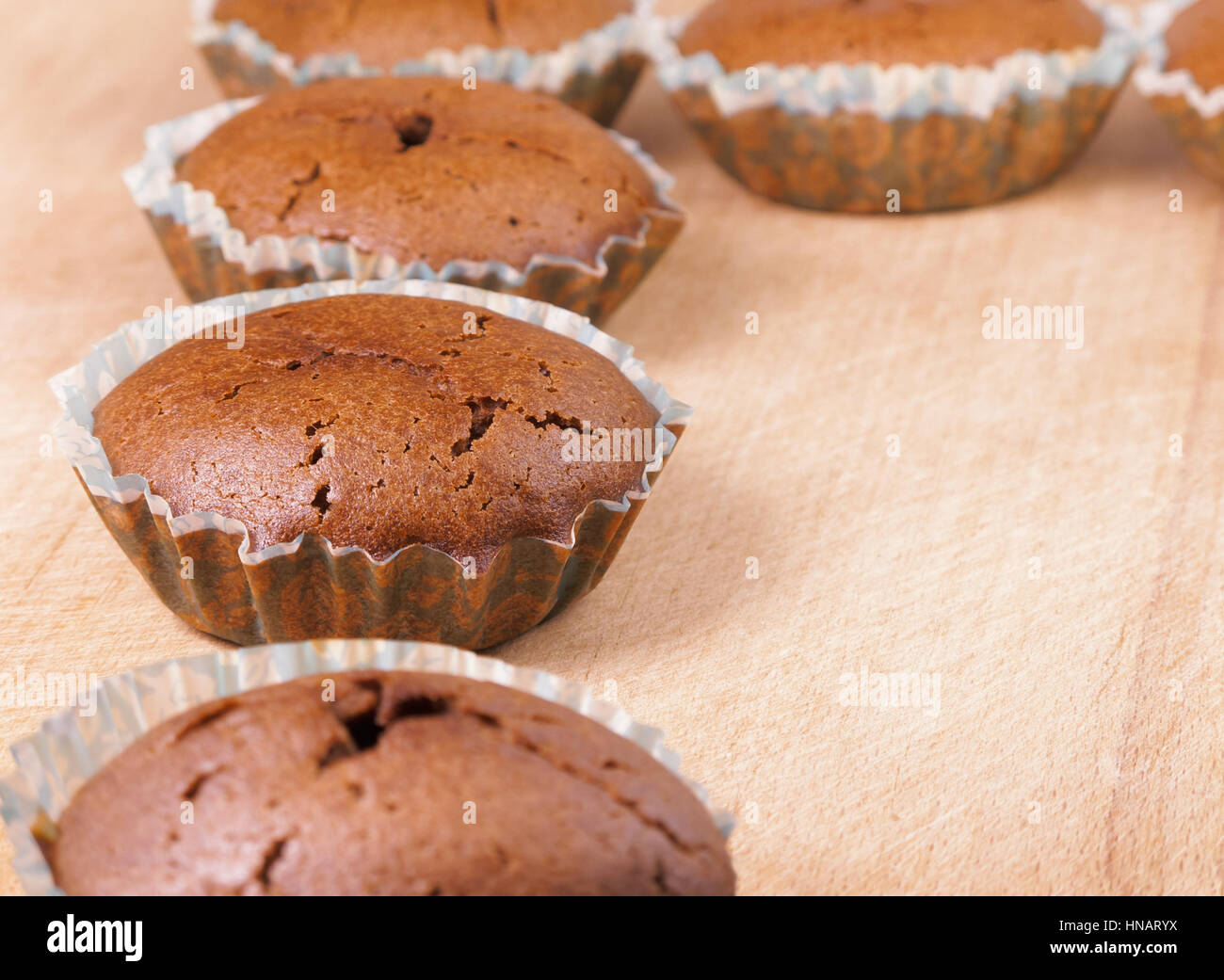 Muffin al cioccolato. Fila di pane appena sfornato muffin al cioccolato in carta in forma di cottura sul pannello di legno Foto Stock