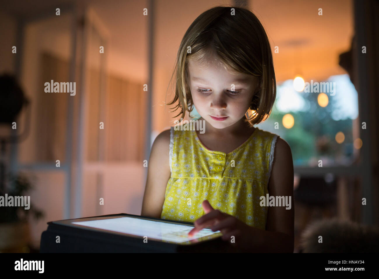 6 anno vecchia ragazza su tablet in serata a casa con la luce che riflette sul suo viso Foto Stock